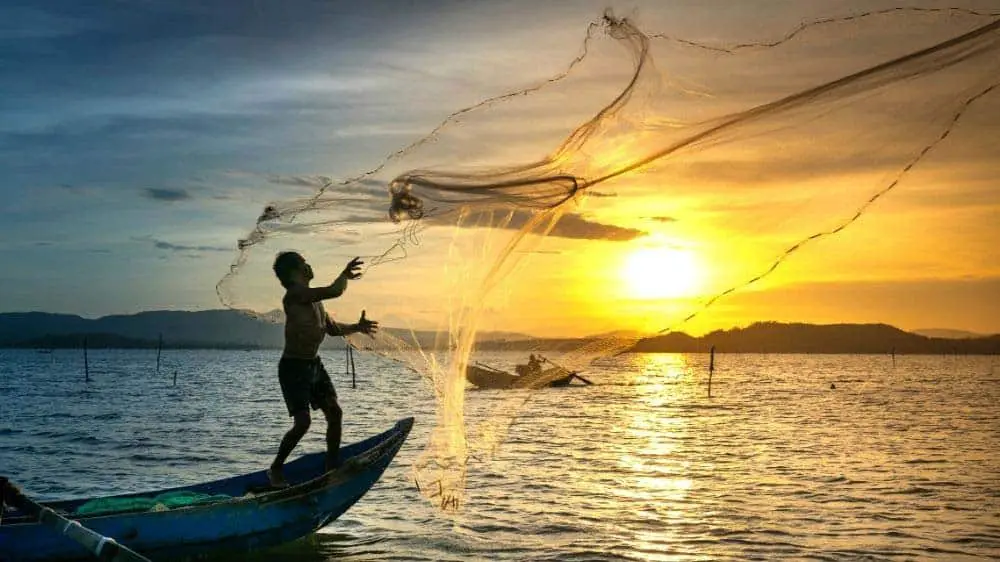 Artisanal fisherman throwing net from a small boat.