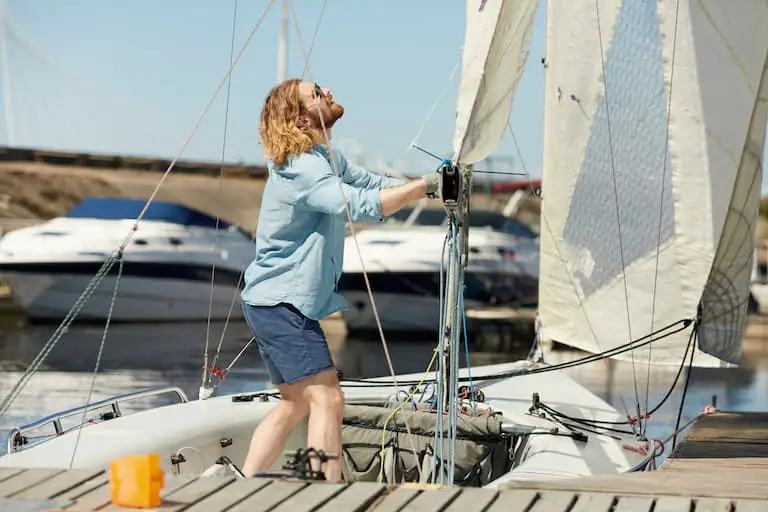 Man lowering sails on boat: Lower the sails to reduce heeling too much