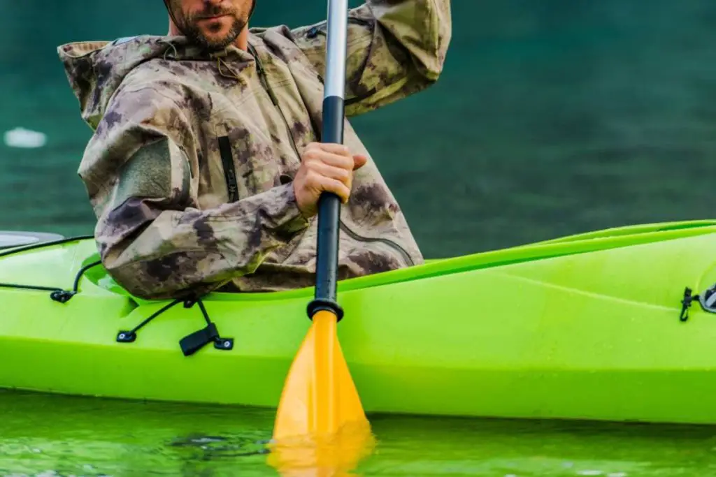 man paddling kayak while wearing rain gear