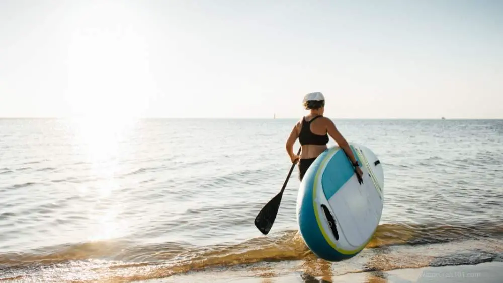 woman carrying an ISUP paddle board into the water